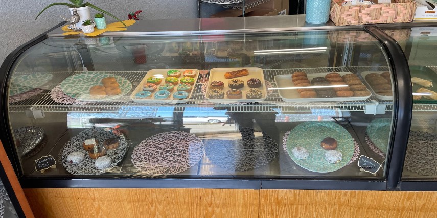 A bakery case filled with a variety of donuts displayed on plates and platters.