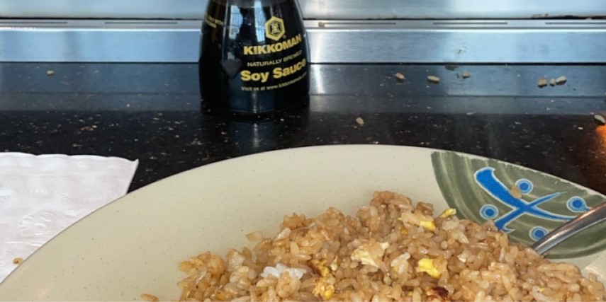 A plate of fried rice with a bottle of Kikkoman soy sauce and a hibachi grill in the background.