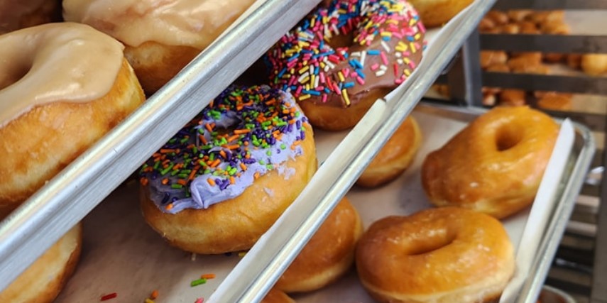 Close-up of racks of donuts. The top level is frosted, the second level is frosted and sprinkled and the third  rack is glazed.