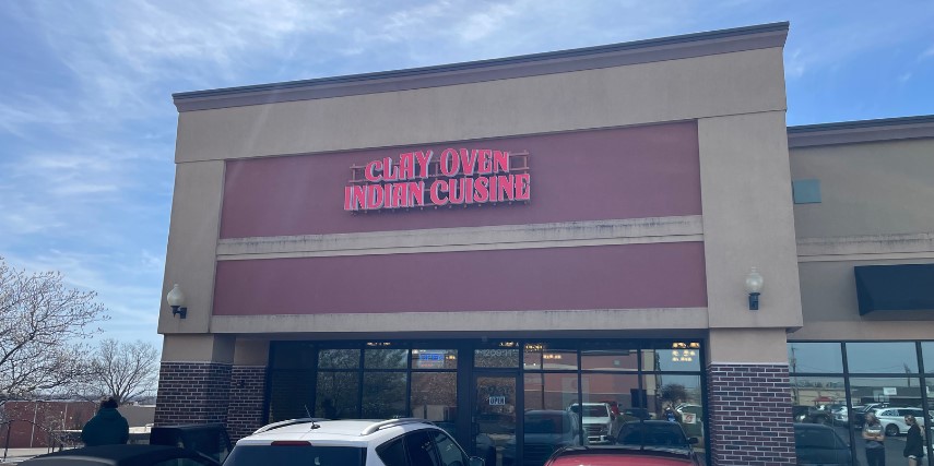 Image of the front of a restaurant. Brown and beige stone and brickwork feature the words, "Clay Oven Indian Cuisine." 