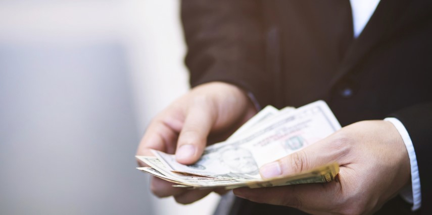 Close-up image of a person dressed in black holding a stack of cash. 