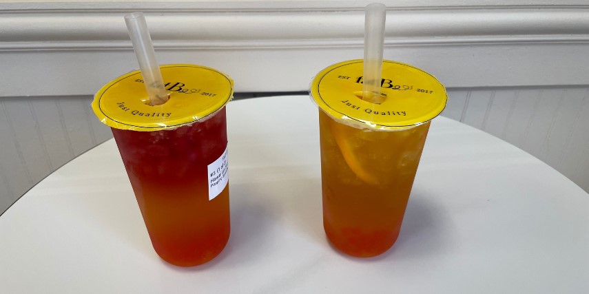 Two disposable cups filled with tea are displayed on a white table.