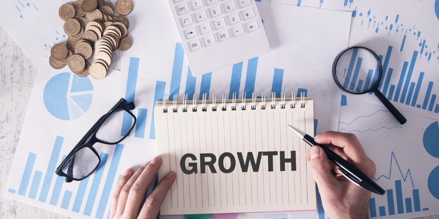 The word "growth" is on a paper tablet. A handful of change, a pair of glasses and a calculator are nearby.