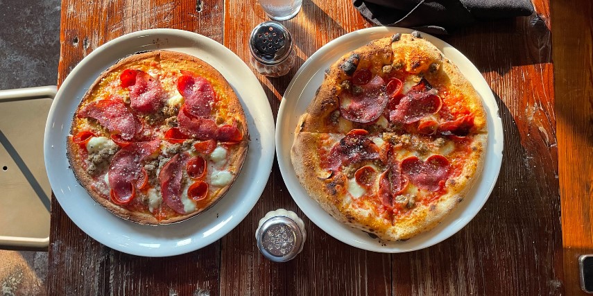 Image of two Neapolitan-style pizzas on white plates surrounded by shakers of parmesan and pepper flakes.