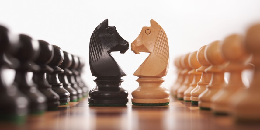 Two chess pieces sit face-to-face on a chess board.
