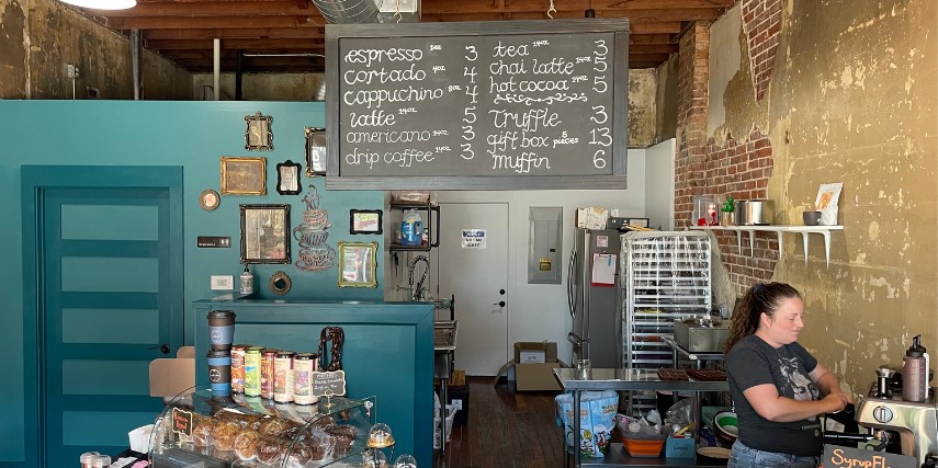 A chalkboard menu hangs in a coffee shop above a bright blue counter.