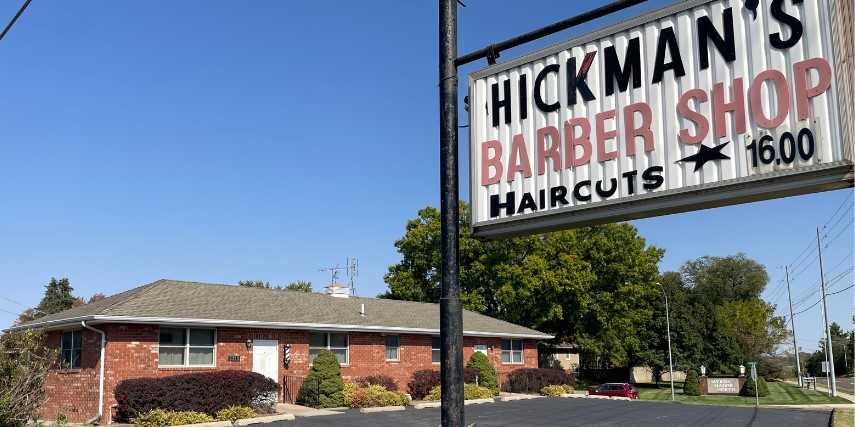 Outside view of Hickman's Barber Shop with sign in the foreground and the building in the distance.