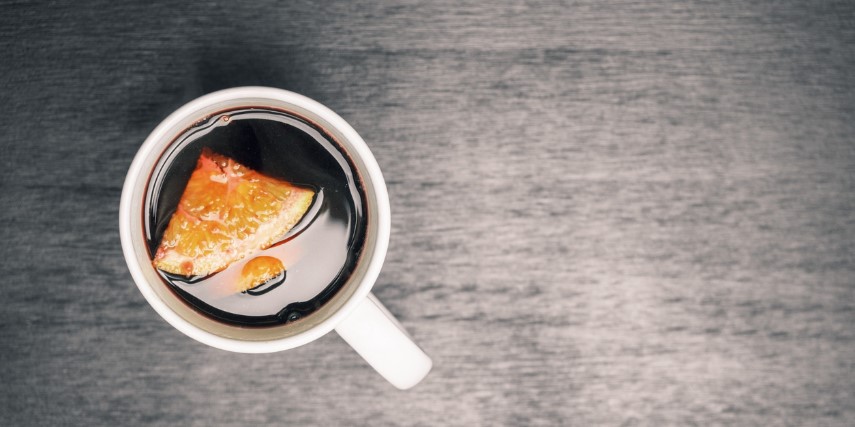 A cup of coffee on a gray table with a piece of pumpkin pie floating in it.