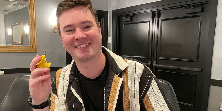 A young smiling man in a striped shirt holds up yellow poker chips.