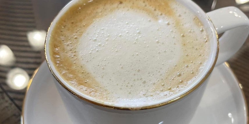 Close up of the frothy surface of a hot coffee drink, served in a white mug.