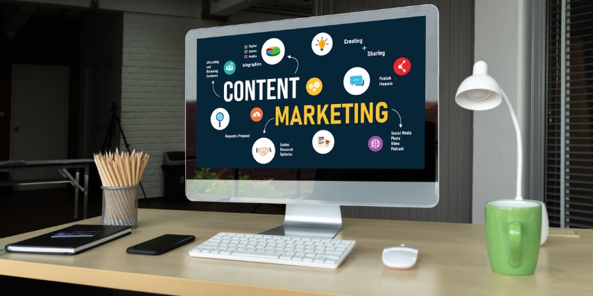 A computer monitor on a desk has "content marketing" and a scattering of graphics on the screen. A mouse, tablet and coffee cup are on the desk, as well.