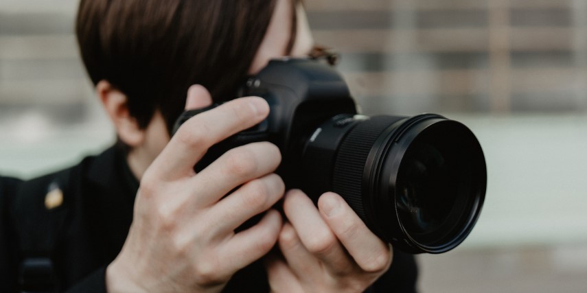 Close-up of a camera held by a professional photographer dressed in black.