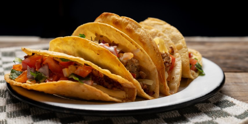 Several tacos sit fanned across a white plate on a table.