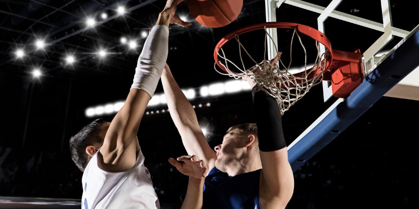 Two basketball players on opposing teams jump for the ball at the basket. 