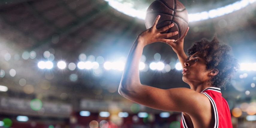 A player attempts to make a shot on the basketball court with bright lights behind him.